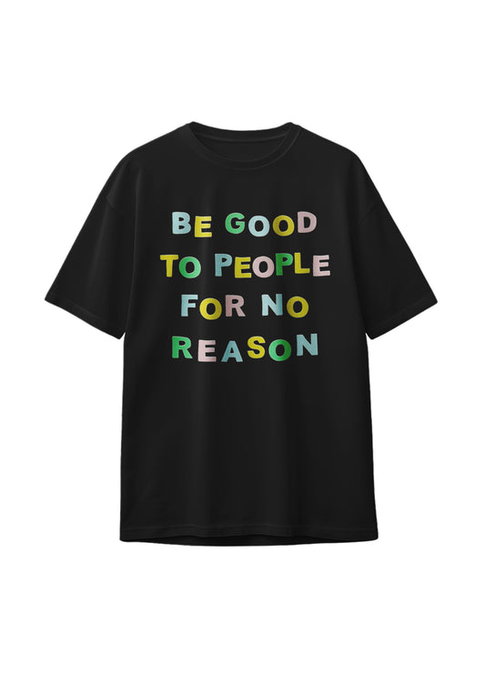Flatlay of black graphic tee with colorful slogan "Be Good to People for No Reason" printed on the front.