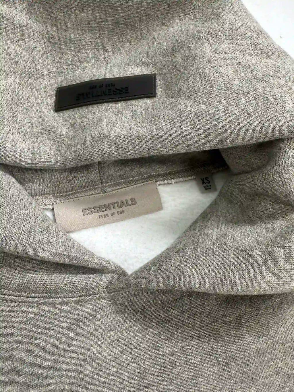 Inner neck detail of ESSENTIALS 2022 fleece hoodie in dark oatmeal color, showing rubber back neck patch and woven size label on oversized streetwear sweatshirt