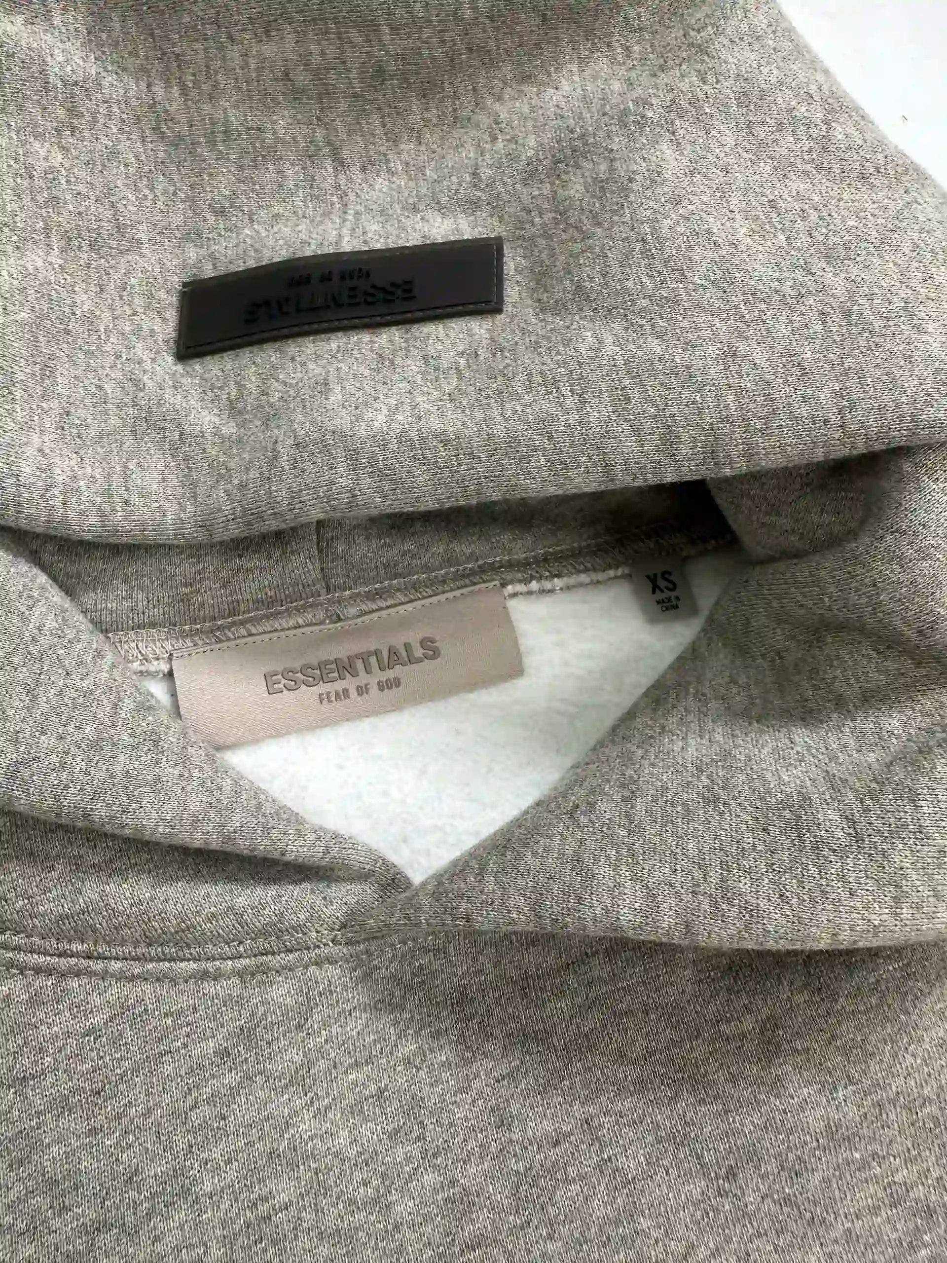 Inner neck detail of ESSENTIALS 2022 fleece hoodie in dark oatmeal color, showing rubber back neck patch and woven size label on oversized streetwear sweatshirt