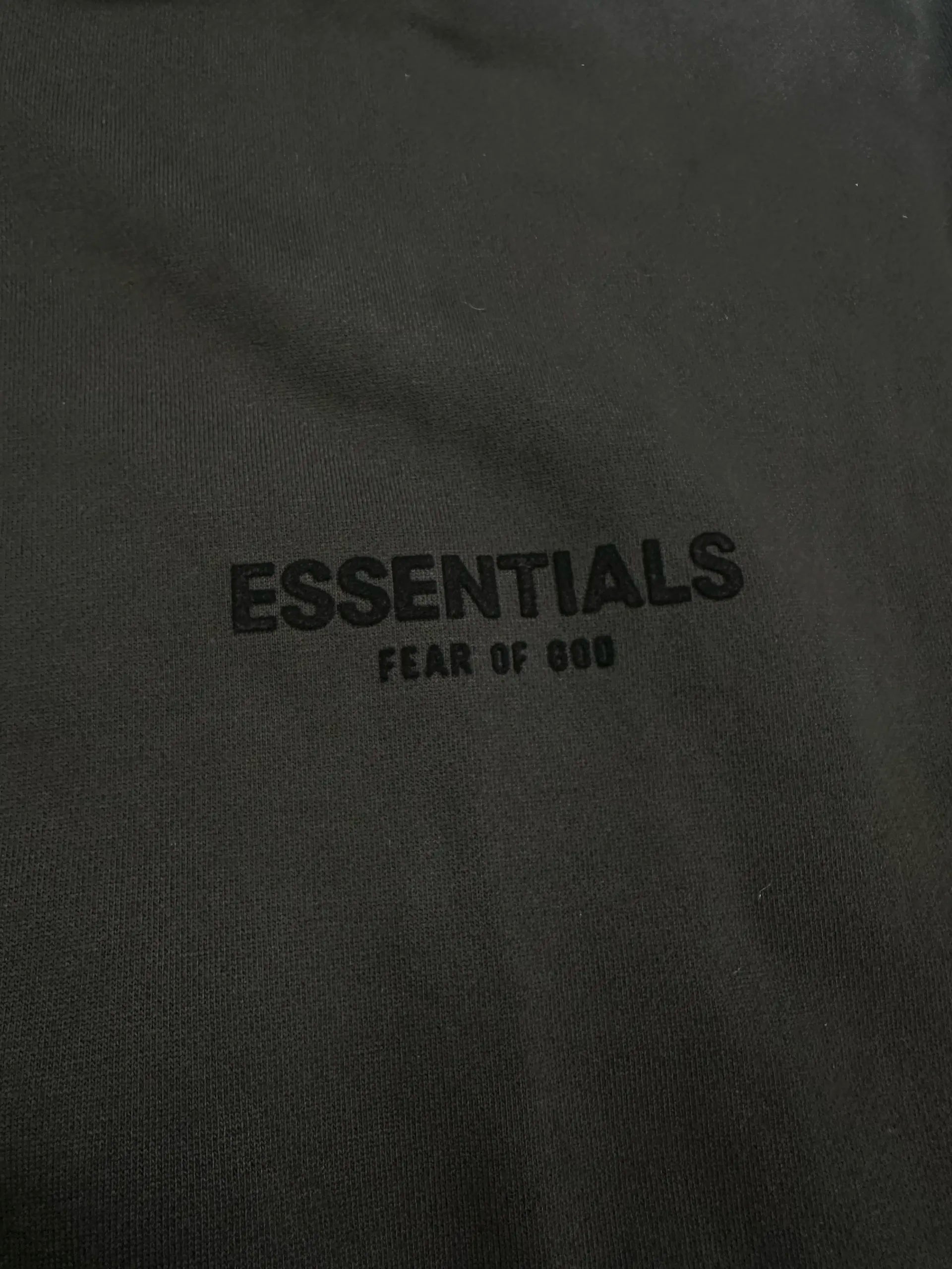 Close-up of front ESSENTIALS Fear of God logo on black hoodie