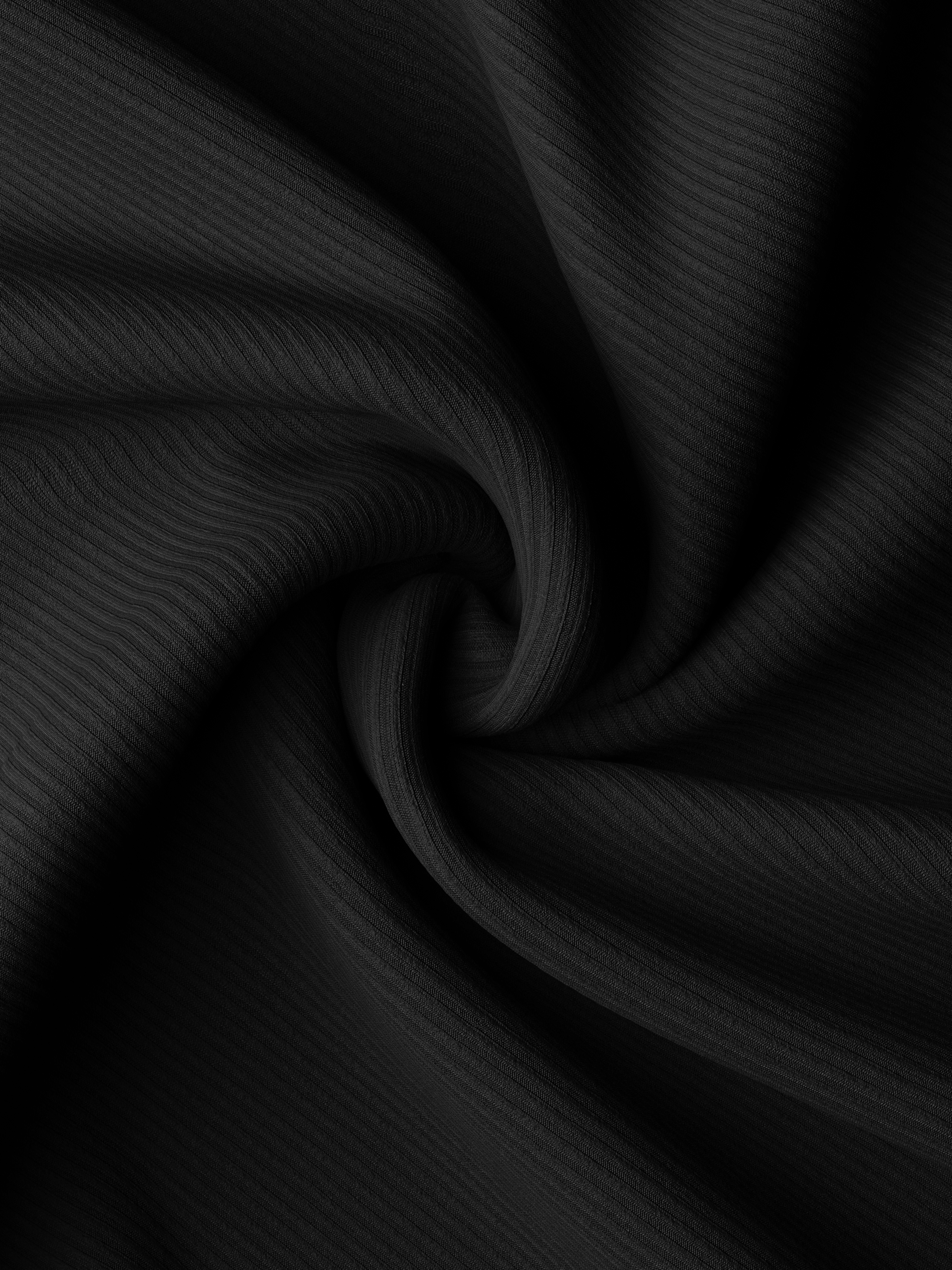 Close-up swirl of black cotton fabric, highlighting texture and softness of graphic tee material.