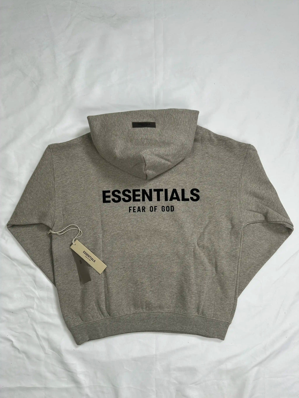Back view of a light heather grey ESSENTIALS hoodie laid flat on a white background, featuring a bold oversized back logo print, relaxed streetwear silhouette, ribbed hem and cuffs, and clean minimalist design suitable for everyday casual wear.